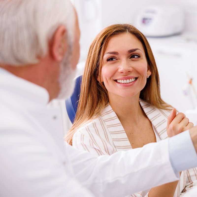 Smiling female dental patient talking to a dentist during consultation at a modern clinic.
