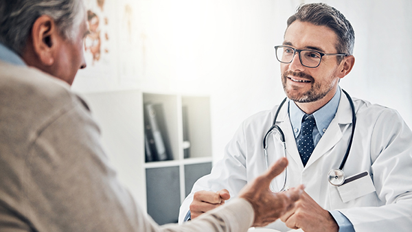 Smiling male doctor discussing treatment plan with elderly patient during consultation.