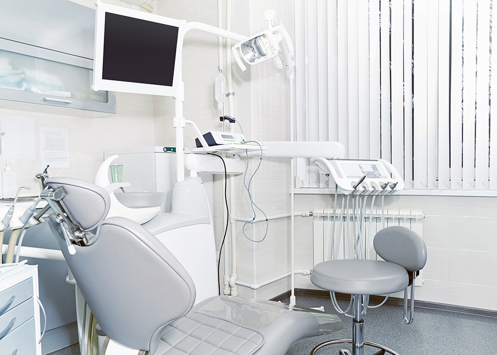 Empty dental operatory with patient chair, overhead light, and dental instruments.