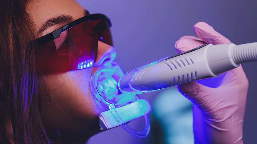 Patient undergoing teeth whitening enhanced by dental laser light and protective glasses